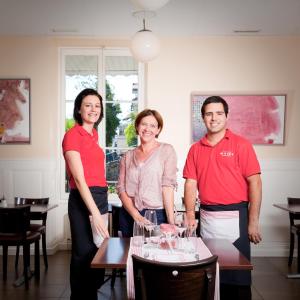 Ein Mann und zwei Frauen stehen neben einem Tisch mit Weingläsern. in der Unterkunft Auberge de la Gare in Grandvaux