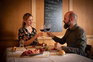 un homme et une femme assis à une table avec des verres à vin dans l'établissement Hotel Restaurant Capricorns, à Wergenstein