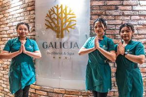 Hotel Galicja Wellness & SPA في أوشفيتز: ثلاث نساء في مئزر أخضر يقفن أمام لافتة