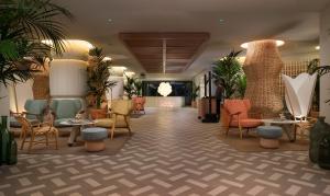 a lobby with chairs and tables and palm trees at ME Sitges Terramar in Sitges