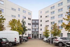 un grand bâtiment blanc avec des voitures garées dans un parking dans l'établissement Vienna House Easy by Wyndham Neckarsulm, à Neckarsulm