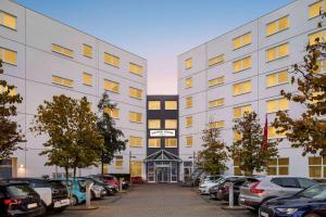 un grand bâtiment blanc avec des voitures garées dans un parking dans l'établissement Vienna House Easy by Wyndham Neckarsulm, à Neckarsulm