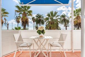 une table et des chaises blanches sur un balcon avec des palmiers dans l'établissement Sitges Seafront Ribera Apartment, à Sitges