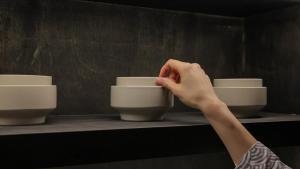 a person holding a cup on a shelf with bowls at Aank Ryokan Yosuriguri Hotel in Cheonan