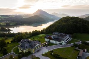 Arabella Jagdhof Resort am Fuschlsee, a Tribute Portfolio Hotel في هوف باي سالزبورج: اطلالة جوية على مبنى على تل بجانب نهر