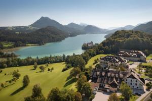 Arabella Jagdhof Resort am Fuschlsee, a Tribute Portfolio Hotel في هوف باي سالزبورج: اطلالة جوية على منزل على تل بجوار بحيرة