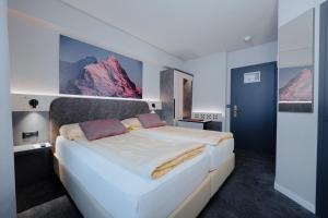 - une chambre avec un grand lit blanc et des montagnes au mur dans l'établissement Hotel Central Wolter - Grindelwald, à Grindelwald