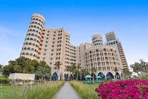 un grand bâtiment avec des fleurs roses devant lui dans l'établissement Al Hamra Residence, à Ras al Khaimah