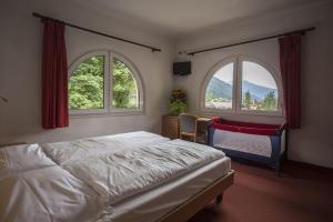 a bedroom with two windows and a bed and a chair at GH Hotel Piaz in Pozza di Fassa