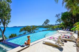 Eine Frau, die neben einem Pool neben dem Wasser sitzt. in der Unterkunft Edge 11 & Free Buggy - Hamilton Island in Hamilton Island