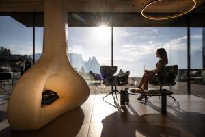 eine Frau auf einem Stuhl in einem Zimmer mit einem großen Fenster in der Unterkunft Hotel Santner Alpine Sport & Relax in Alpe di Siusi