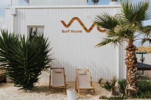 twee stoelen en een palmboom voor een surfhuis bij We Surf House in Figueira da Foz