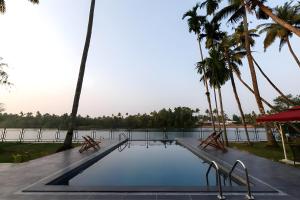 コーチにあるLhasa Ayurveda and Wellness Resort - A BluSalzz Collection, Kochi, Keralaのヤシの木とベンチ2つが備わるスイミングプール