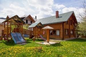 une maison en rondins avec une aire de jeux dans la cour dans l'établissement Садиба У Василини та Романа, à Bukovel