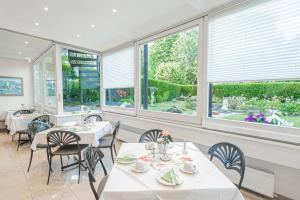 un comedor con mesas y sillas blancas y ventanas en Hotel Villa am Kurpark, en Bad Homburg vor der Höhe