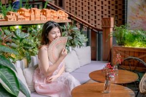 una chica sentada en un sofá sosteniendo un ventilador en Seahorse Han Market Da Nang Apartment by Haviland, en Da Nang