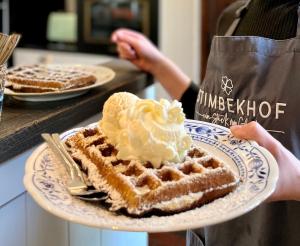 una persona sosteniendo un plato de gofre con crema batida en Stimbekhof, en Bispingen