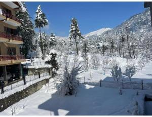 a snow covered yard with trees and a building at Pine Shadow Retreat, Manali in Manāli