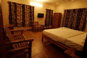 1 dormitorio con cama, sillas y cortinas en The Alpine Inn, en Gūdalūr