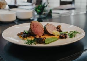 a white plate with meat and vegetables on a table at Hotel Horal in Rožnov pod Radhoštěm