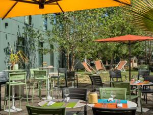 un patio esterno con tavoli, sedie e ombrelloni di Novotel Paris Coeur d'Orly Airport a Orly