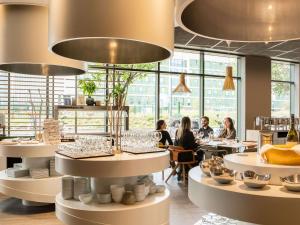 un ristorante con persone sedute ai tavoli in una stanza con ampie finestre di Novotel Paris Coeur d'Orly Airport a Orly