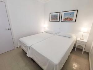 ein weißes Bett in einem weißen Zimmer mit zwei Bildern an der Wand in der Unterkunft Bayuca 107 Yumbo Center By Pride Holiday Rentals in Maspalomas