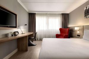 Ramada by Wyndham Amsterdam Airport Schiphol في باتهوفيدورب: غرفة بالفندق سرير وكرسي احمر