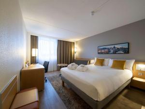 a hotel room with a large bed and a desk at Novotel Maastricht in Maastricht