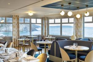 een restaurant met tafels, stoelen en ramen bij Hôtel Morgat Le Grand Hôtel De La Mer in Crozon