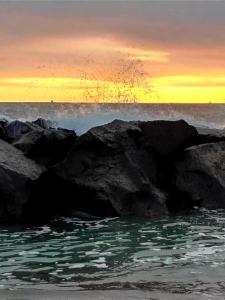 a sunset over the ocean with rocks in the water at Sweet Home FCO Airport Roma in Fiumicino