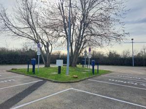 een parkeerplaats met blauwe parkeermeters en een boom bij Hotel Le Saint Vincent Lyon Sud in Vourles