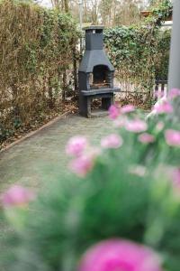 a outdoor oven in a garden with pink flowers at Chalet op familiepark Veluws Hof op de Hoge Veluwe in Hoenderloo