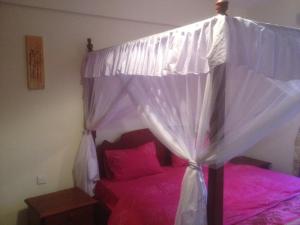 um quarto com uma cama de dossel com lençóis cor-de-rosa em Bamburi Beach Homes em Bamburi