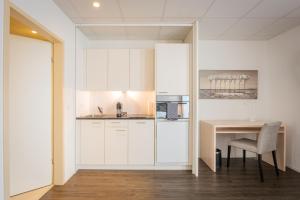 a kitchen with white cabinets and a table with a chair at Los Lorentes Apartments Bern Airport in Belp