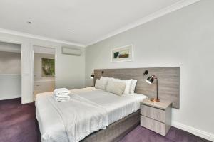 a white bedroom with a large bed and a lamp at Villa 3br Chardonnay Villa located within Cypress Lakes Resort in Pokolbin