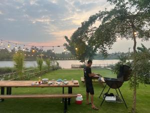 mężczyzna stojący obok grilla obok stołu piknikowego w obiekcie Bình An lake view w mieście Buôn Ma Thuột