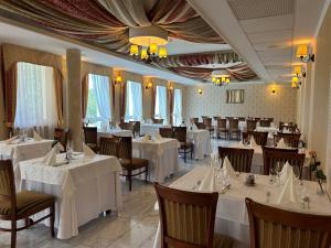 un restaurante con mesas y sillas blancas y ventanas en Calimbra Wellness Hotel Superior, en Miskolctapolca