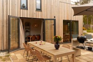 een patio met een houten tafel en stoelen bij Dutchen Zeegser Duinen Villalodges in Zeegse