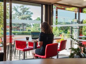 une femme assise à une table avec un ordinateur portable dans l'établissement ibis Colmar Est - Hotel Restaurant en Alsace, à Colmar