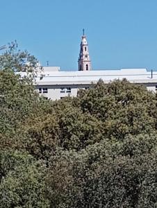 Un edificio con una torre dell'orologio dietro alcuni alberi di Casa Talika a Fátima