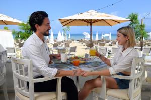 un homme et une femme assis à une table sur la plage dans l'établissement Cavomarina Beach- Adults Only, à Kavos