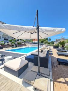 - une piscine avec un parasol blanc et des chaises dans l'établissement Apartments Silva with a view of sea, à Trogir