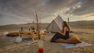 una mujer sentada en una manta en el desierto con una tienda en Duna Camp Huacachina, en Ica