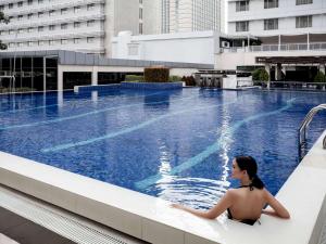 Eine Frau, die auf einem Felsvorsprung neben einem Pool sitzt. in der Unterkunft Pullman Jakarta Indonesia in Jakarta