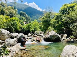 een man zit op rotsen in een rivier bij Hostel 360 Degree in Manāli