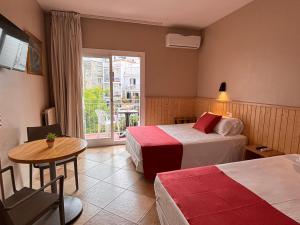 Cette chambre comprend deux lits, une table et une fenêtre. dans l'établissement Hotel Piccadilly Sitges, à Sitges