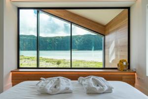 een slaapkamer met een groot raam en handdoeken op een bed bij Sete Cidades Lake Cabin - Casa da Lagoa in Ponta Delgada