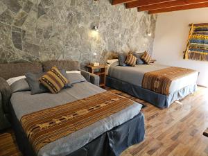 sypialnia z 2 łóżkami i kamienną ścianą w obiekcie Lodge Quelana w mieście San Pedro de Atacama