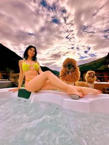 uma mulher sentada à beira de uma piscina com dois cães em Nira Mountain Resort Futura em Valdidentro